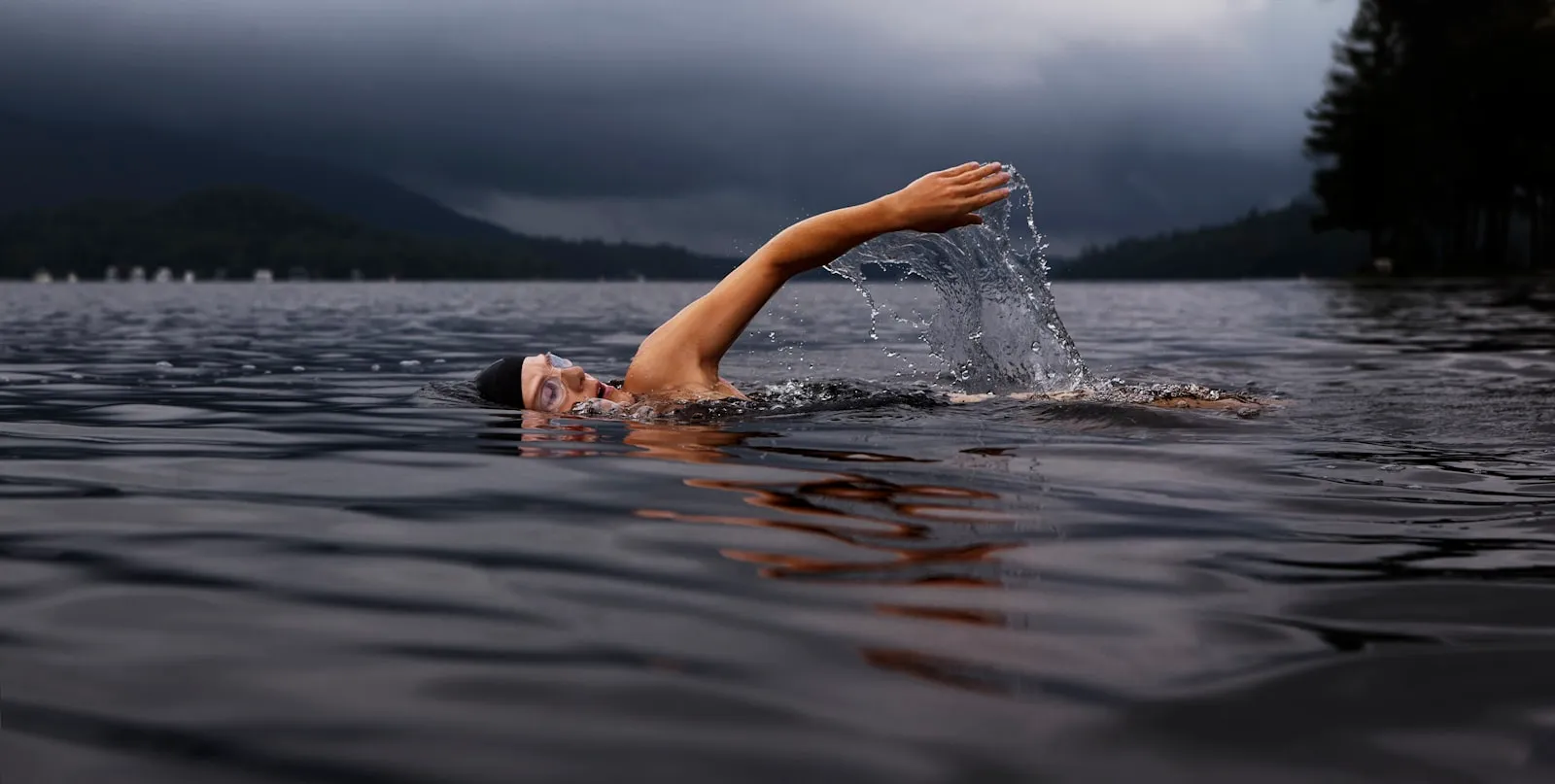 An open-water swimmer mid-stroke on a dark lake.