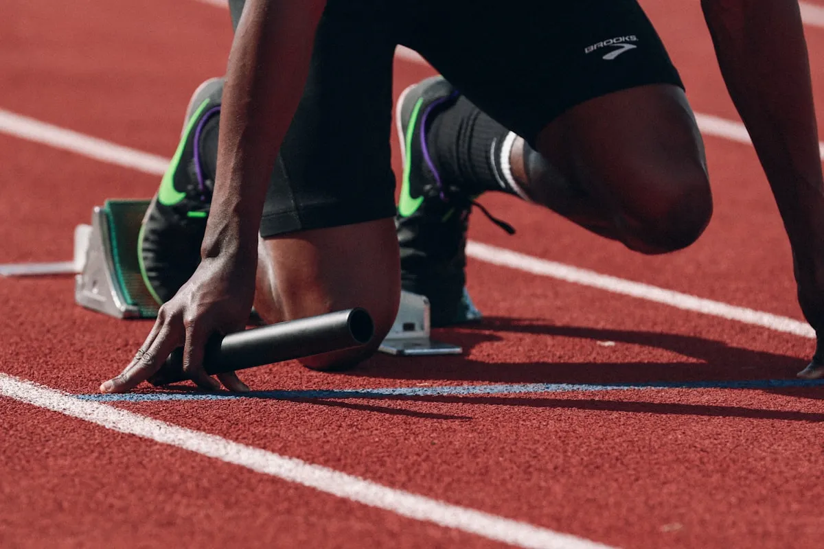 A relay runner crouched at the start line, baton in hand.