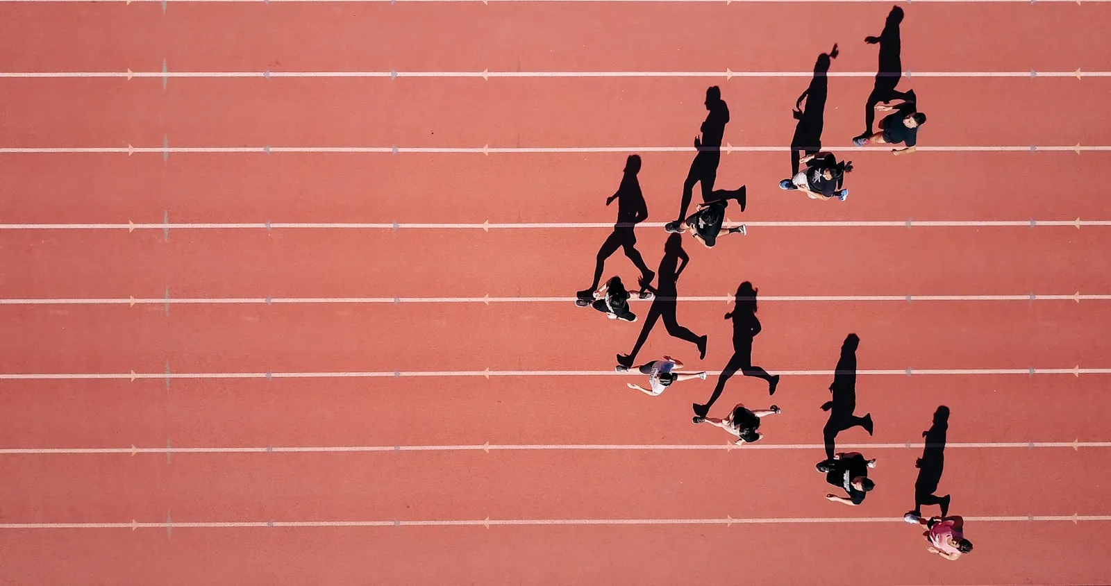 A running track from above, athletes casting long shadows across the lanes.